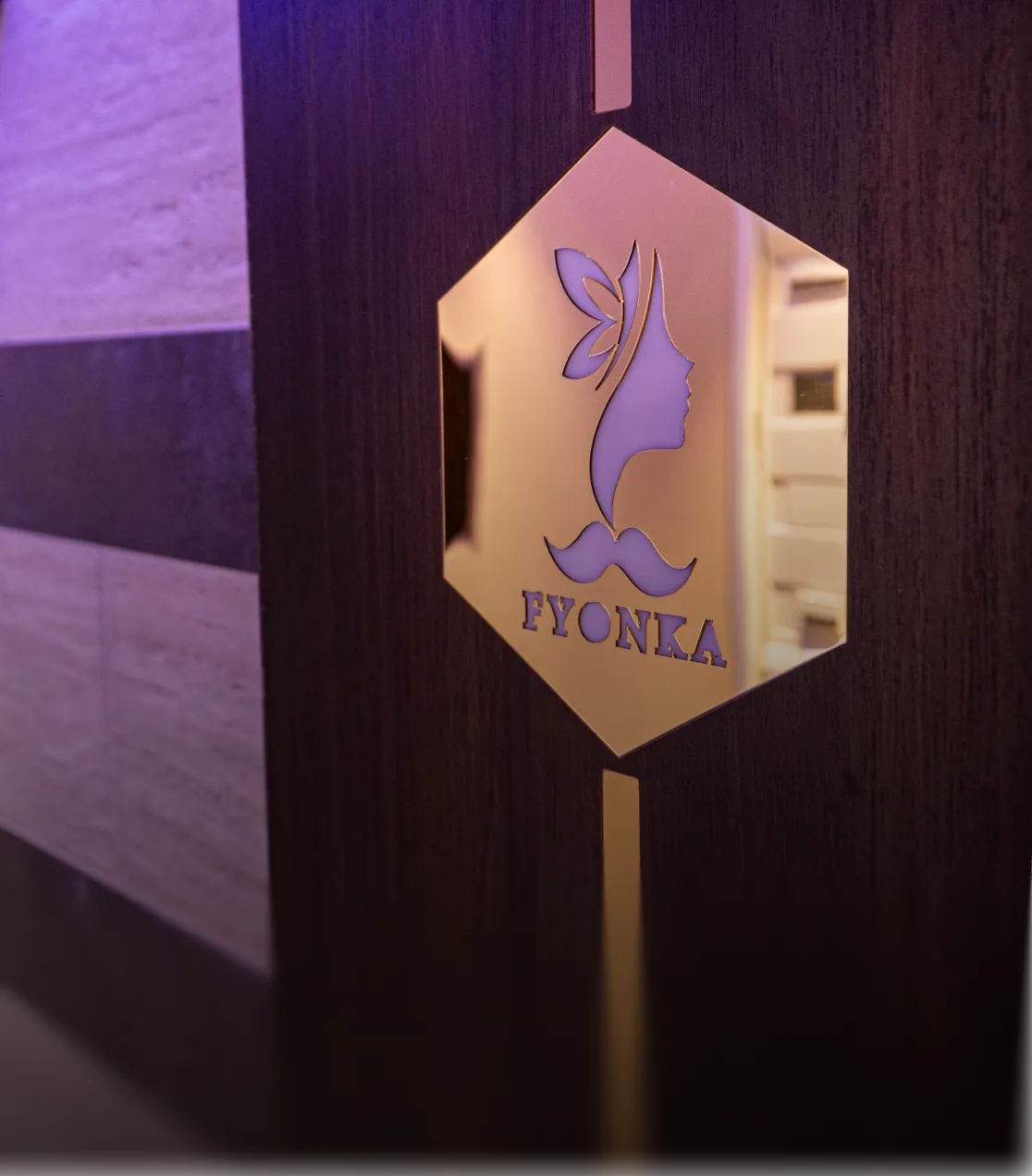 Goldfarbenes sechseckiges Schild an einer Holztür mit dem Logo eines Frauenprofils mit Schmetterlingsflügeln und der Aufschrift FYONKA.