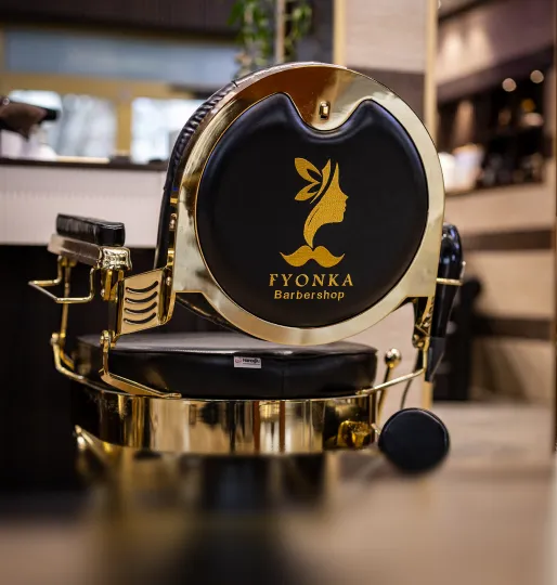 Schwarzer und goldener Friseurstuhl mit Logo und Schriftzug 'FYONKA Barbershop' im Inneren eines Friseursalons.