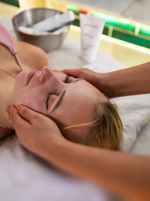 Frau, die eine Gesichtsmassage erhält, mit geschlossenen Augen, Hände des Therapeuten auf ihrem Gesicht.