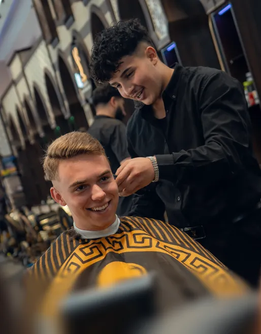 Fröhlicher Friseur schneidet die Haare eines jungen Mannes in einem modernen Friseursalon.