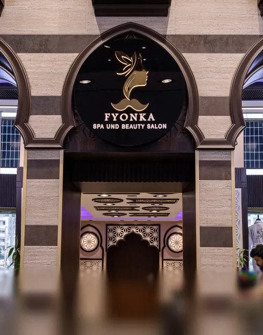 Eingang eines Spa- und Schönheitssalons mit dem runden Schild 'FYONKA SPA UND BEAUTY SALON' vor einer Wand mit dekorativen Bögen.