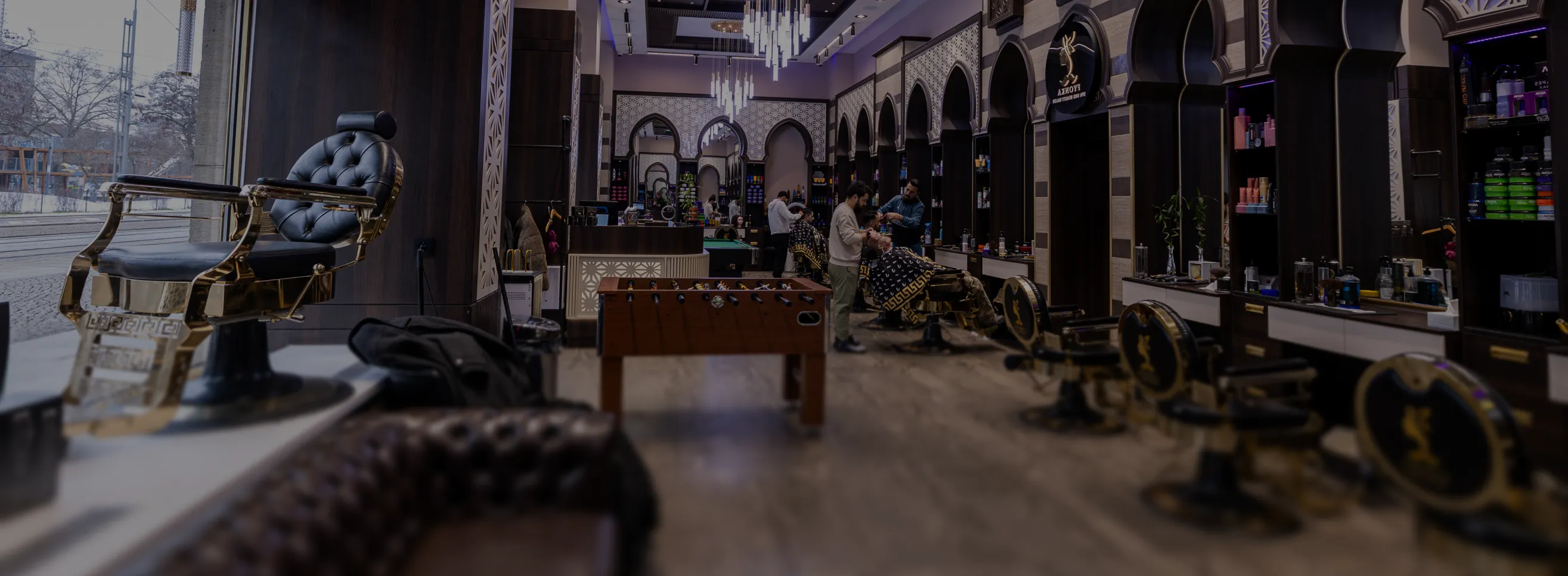 Luxuriöse Barbershop-Interieur mit Friseurstühlen, Kunden und einem Kickertisch in der Mitte.