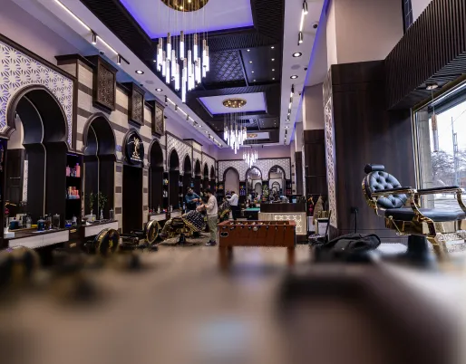 Moderne Barbershop mit dunklem Holzinterieur, stilvollen Pendelleuchten und Friseurstühlen, in dem Kunden bedient werden.