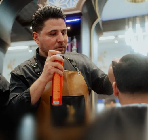 Friseur hält ein Haarspray in der Hand und stylt die Haare eines Kunden in einem Salon.