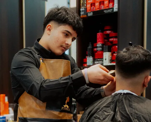 Ein Friseur mit brauner Schürze schneidet einem Kunden die Haare in einem Friseursalon.