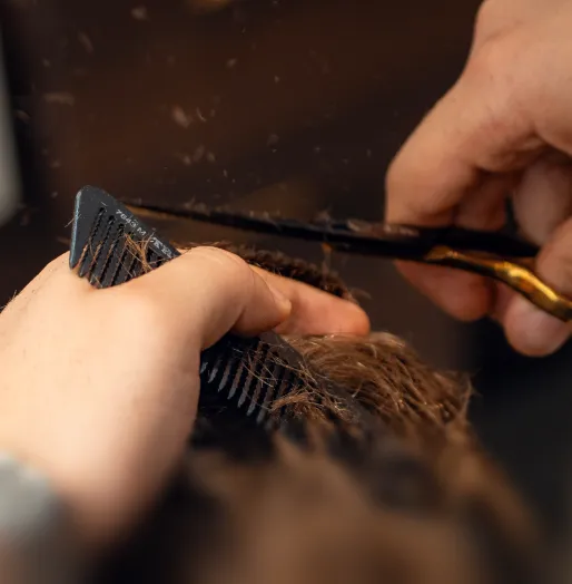 Nahaufnahme von Händen, die Haare mit einem Kamm und einer Schere schneiden.