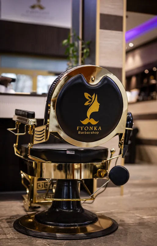 Luxuriöser Friseurstuhl mit goldenem Rahmen und schwarzer Polsterung, Logo von Veluna Wellness House Barbershop auf der Rückenlehne.