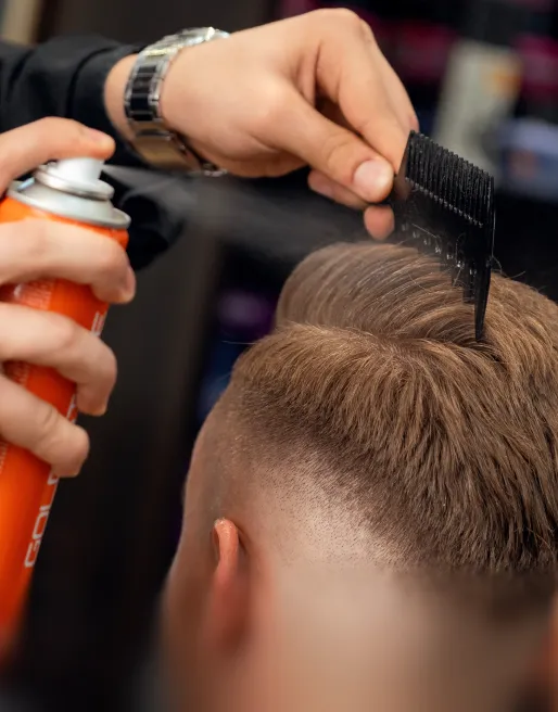 Friseur sprüht Haarspray auf einen frisch geschnittenen Herrenhaarschnitt und kämmt das Haar.