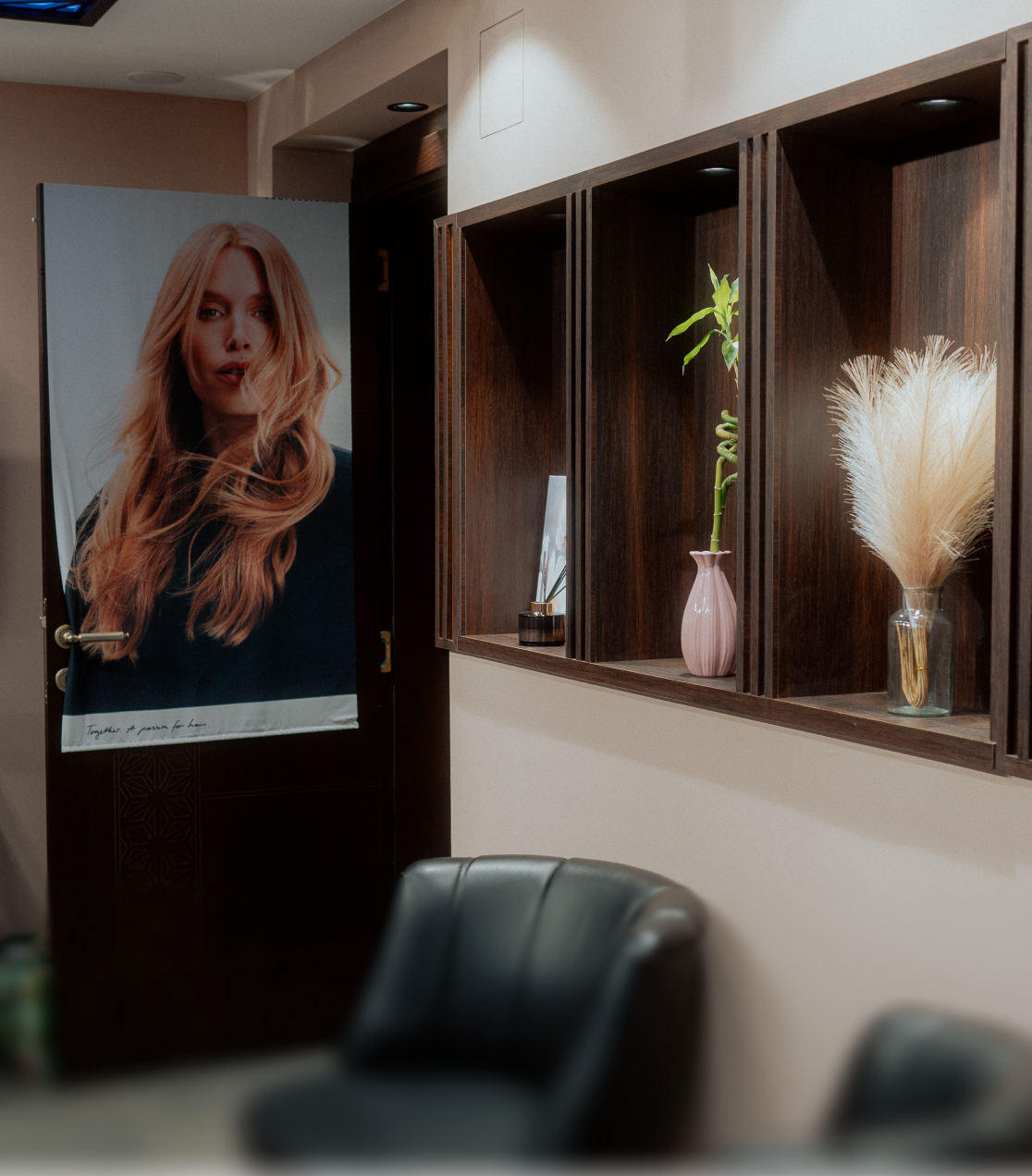 Saloninterieur mit einem Poster einer Frau mit langem, roten Haar an der Tür und Wandregalen mit dekorativen Vasen und Pflanzen.