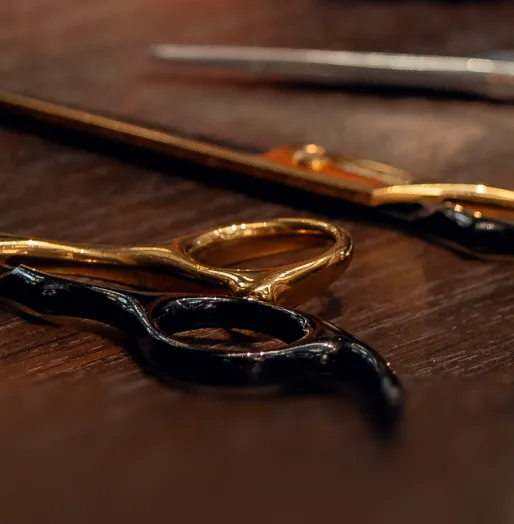 Nahaufnahme von goldenen und schwarzen Haarschneidescheren auf einem braunen Holztisch.