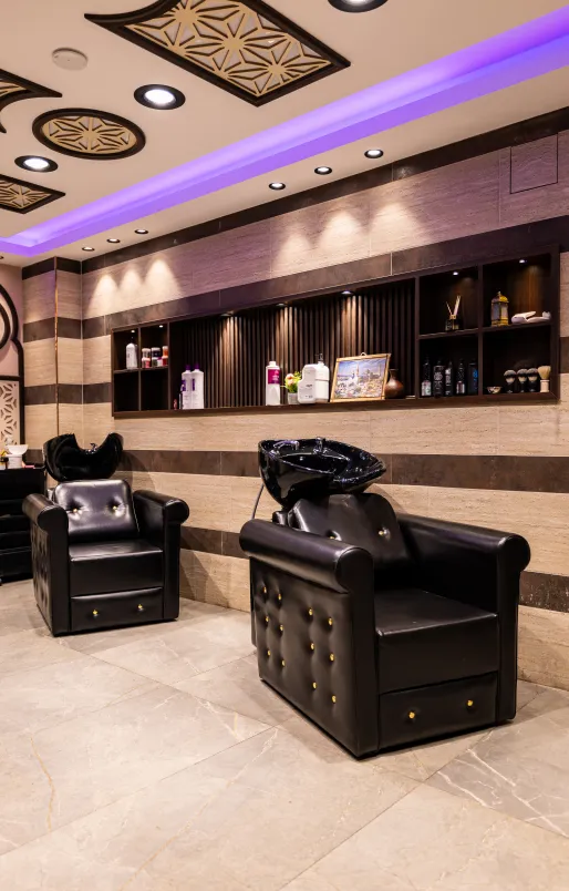 Moderne Friseursalon-Waschstation mit zwei schwarzen, gepolsterten Sesseln und eingebauten Waschbecken unter beleuchteten Regalen.