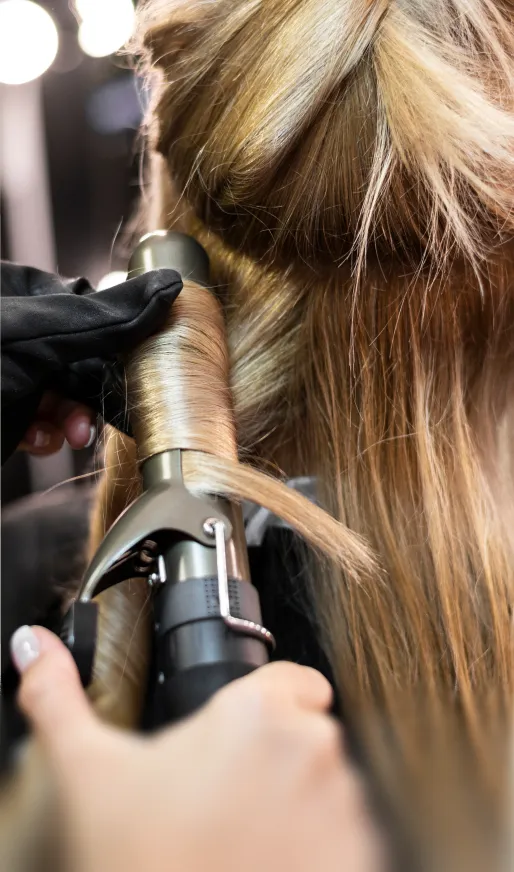 Nahaufnahme einer Person, die blonde Haare mit einem Lockenstab lockt.