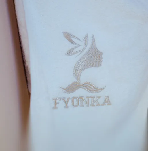 Nahaufnahme eines weißen Stoffes mit einem gestickten Profil einer Frau mit Blättern als Haaren und dem Text 'FYONKA'.