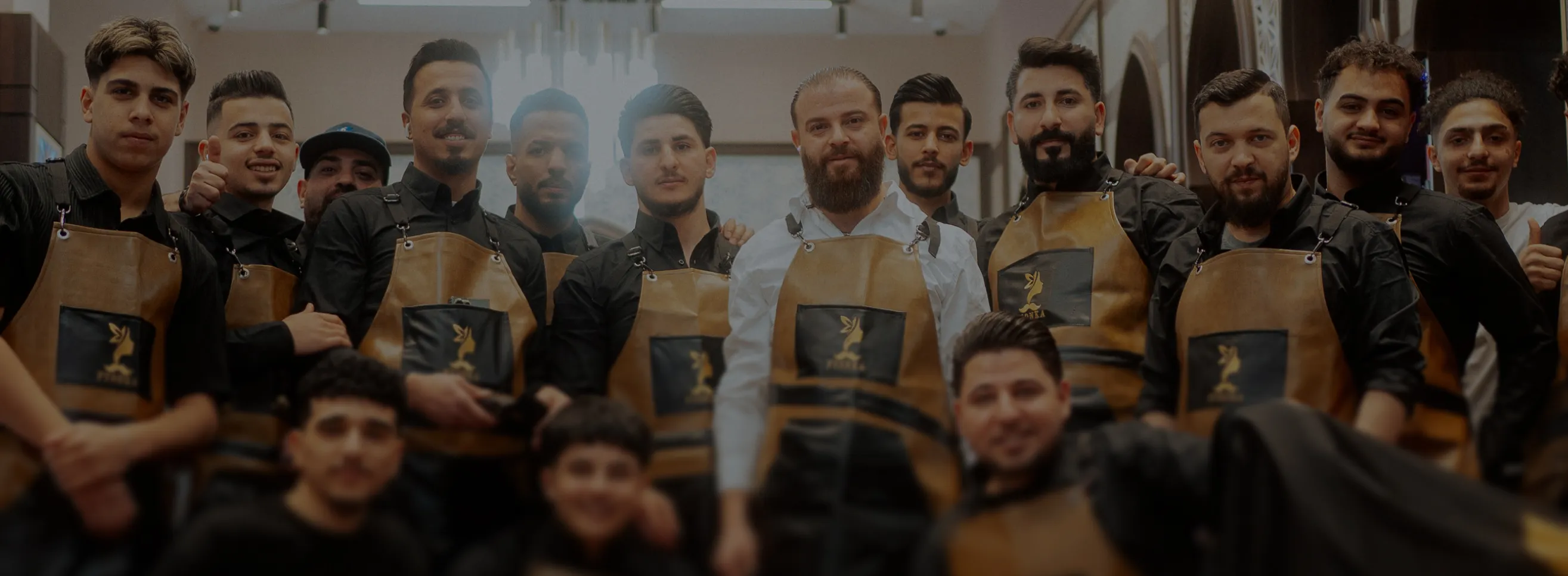 Gruppenfoto von männlichen Friseuren mit braunen Lederschürzen in einem Salon.